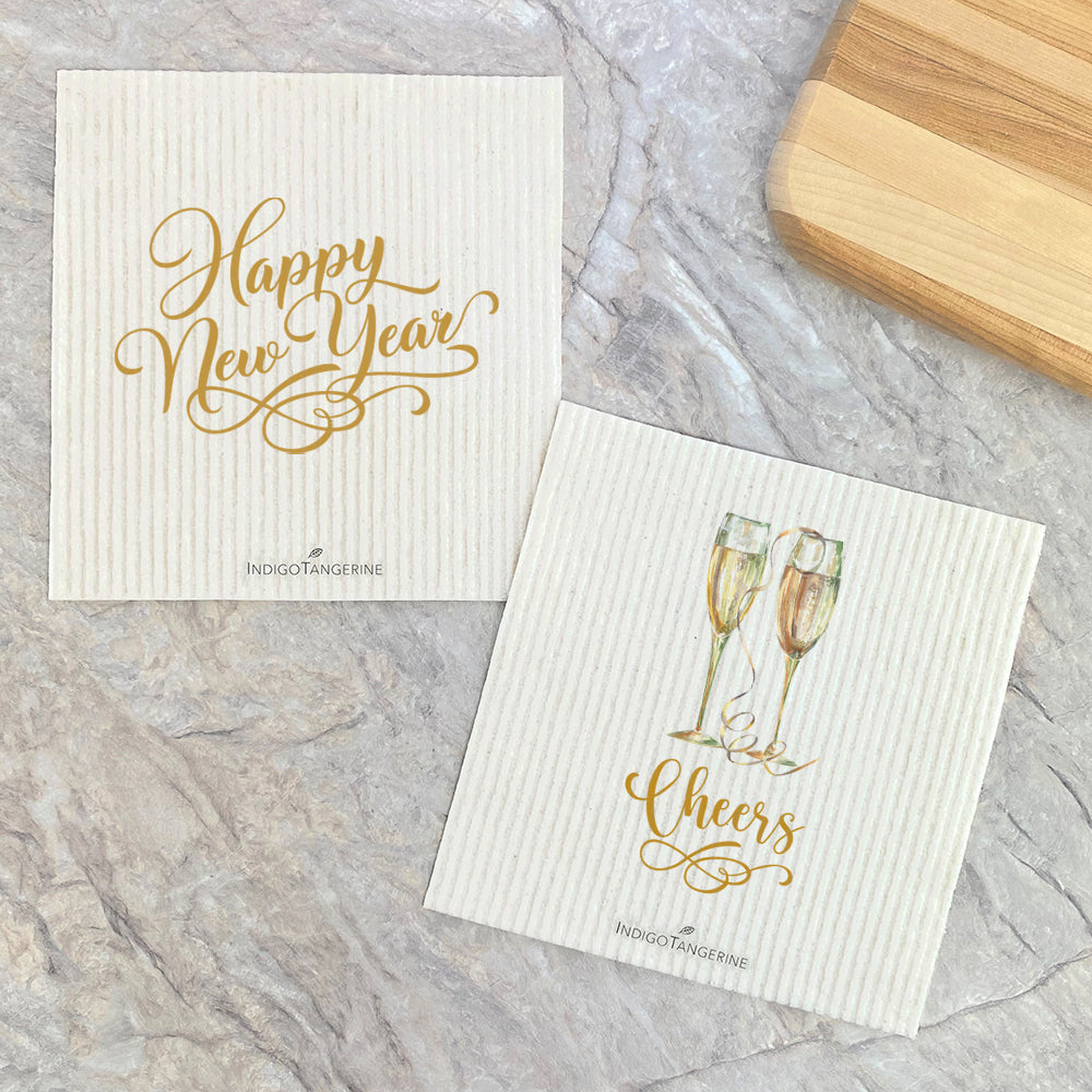 Two Swedish dish cloths featuring a gold script design that reads 'Champagne Cheers, Happy New Year', eco-friendly and reusable.