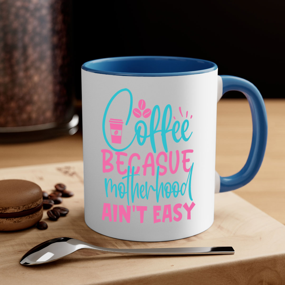 A stylish two-tone coffee mug with a colored handle and glossy finish, featuring the phrase 'Coffee Because Motherhood Ain't Easy'.