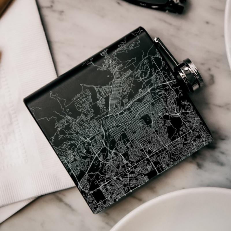 Custom engraved matte black hip flask featuring a map of Colorado Springs, Colorado, with coordinates, alongside a canvas bag and funnel.