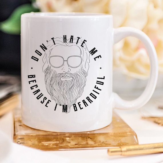 A humorous coffee mug with the phrase 'Don't Hate Me Because I'm Beardiful' printed on it, showcasing a fun design perfect for coffee lovers.