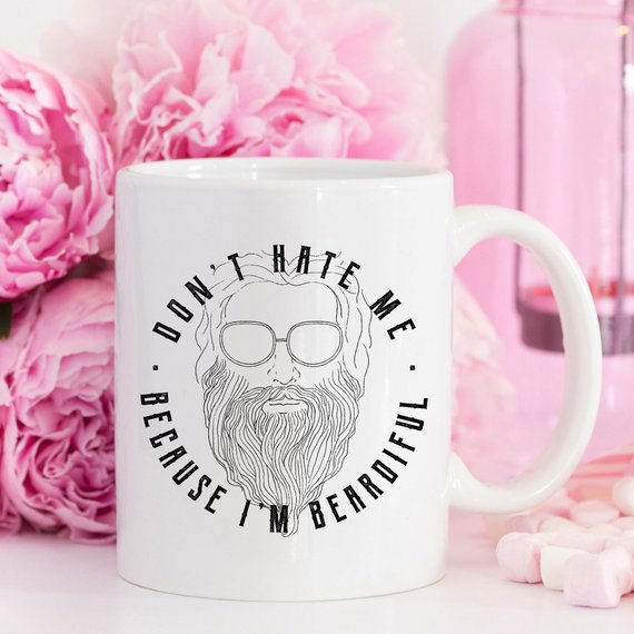 A humorous coffee mug with the phrase 'Don't Hate Me Because I'm Beardiful' printed on it, showcasing a fun design perfect for coffee lovers.