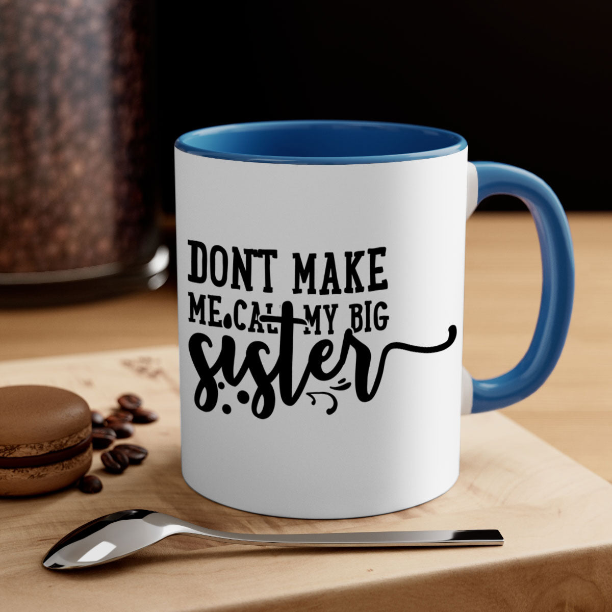 A two-tone ceramic coffee mug with the phrase 'Don't Make Me Call My Big Sister' printed on it, featuring a colored handle and glossy finish.