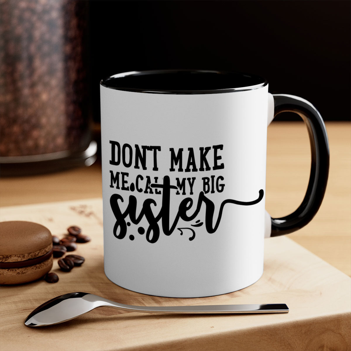 A two-tone ceramic coffee mug with the phrase 'Don't Make Me Call My Big Sister' printed on it, featuring a colored handle and glossy finish.