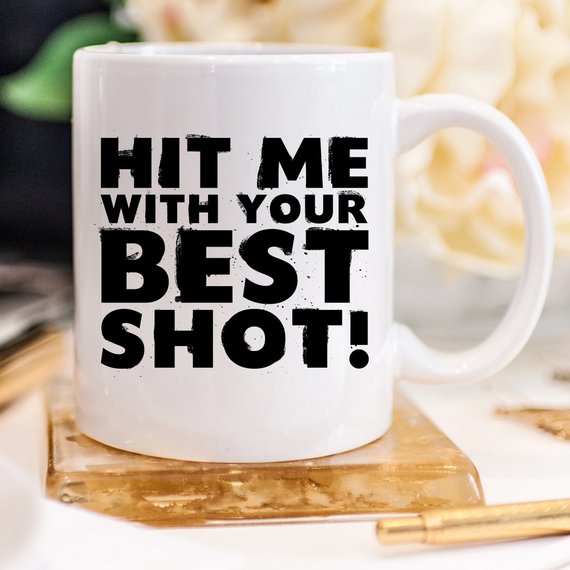 Funny Coffee Mug with 'Hit Me With Your Best Shot' design, crafted from high-grade ceramic, showcasing vibrant print on both sides.