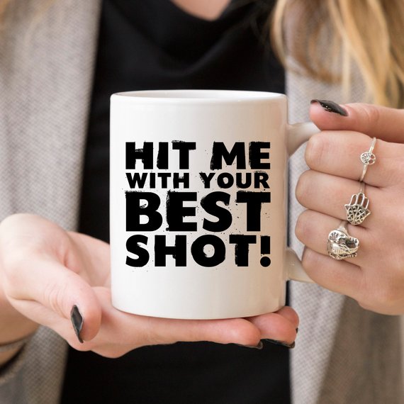 Funny Coffee Mug with 'Hit Me With Your Best Shot' design, crafted from high-grade ceramic, showcasing vibrant print on both sides.