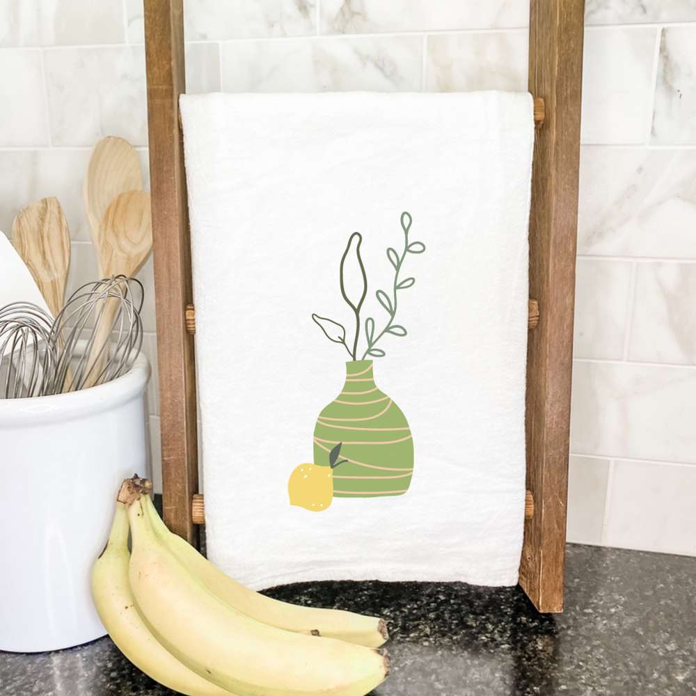 A vibrant green vase with lemons design on a cotton tea towel, showcasing its absorbent texture and hemmed edges.