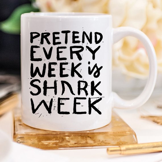 A humorous coffee mug featuring the phrase 'Pretend Every Week Is Shark Week', designed with a playful shark graphic, perfect for coffee lovers.
