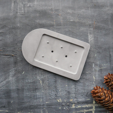 A self-drying soap dish made from eco-friendly diatomite, featuring a concrete-like finish with drainage holes for quick drying.