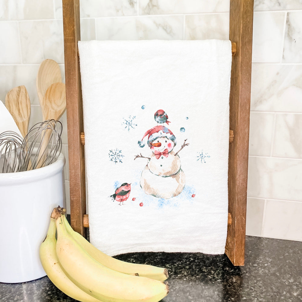 A charming cotton tea towel featuring a snowman surrounded by colorful birds, perfect for festive kitchen decor.