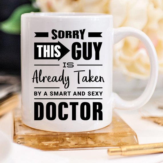 A humorous coffee mug with the phrase 'Sorry This Guy Is Already Taken By A Smart And Sexy Doctor' printed on it, showcasing a fun design.