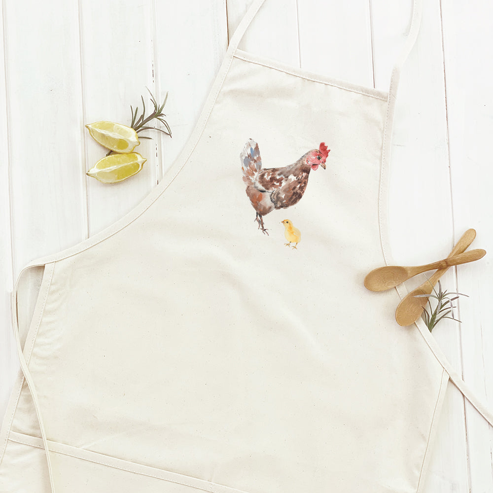A stylish women's apron featuring a watercolor hen and chick design, made from durable cotton canvas with natural twill ties.