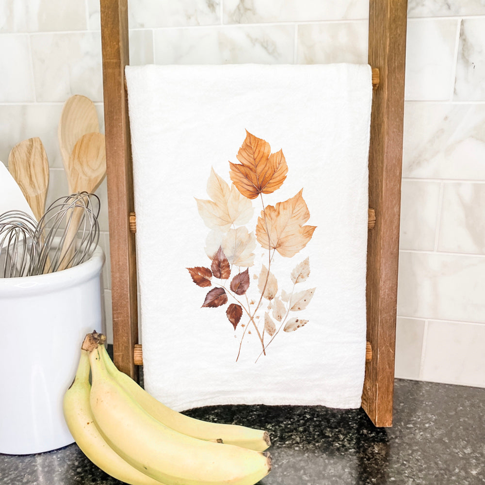 A vibrant watercolor leaf bouquet design on a cotton tea towel, showcasing its absorbent texture and hemmed edges.