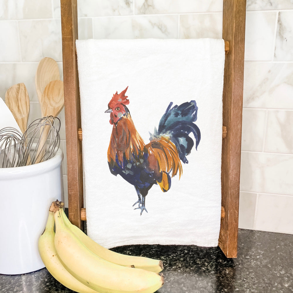 A vibrant watercolor rooster design on a cotton tea towel, showcasing its absorbent fabric and hemmed edges.