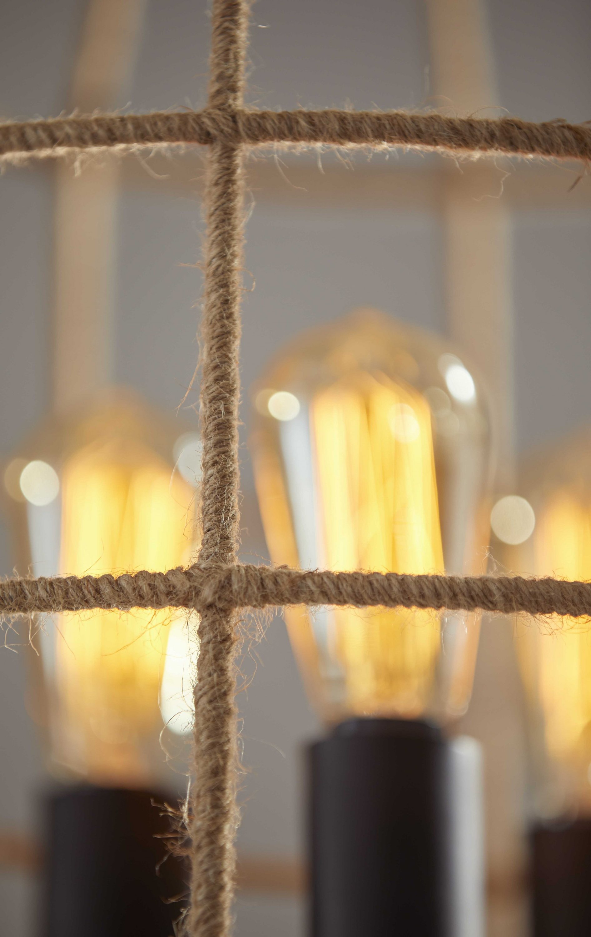 A modern black shade floor lamp with a tripod base, featuring a metal wire cage wrapped in rope and three vintage Edison bulbs.