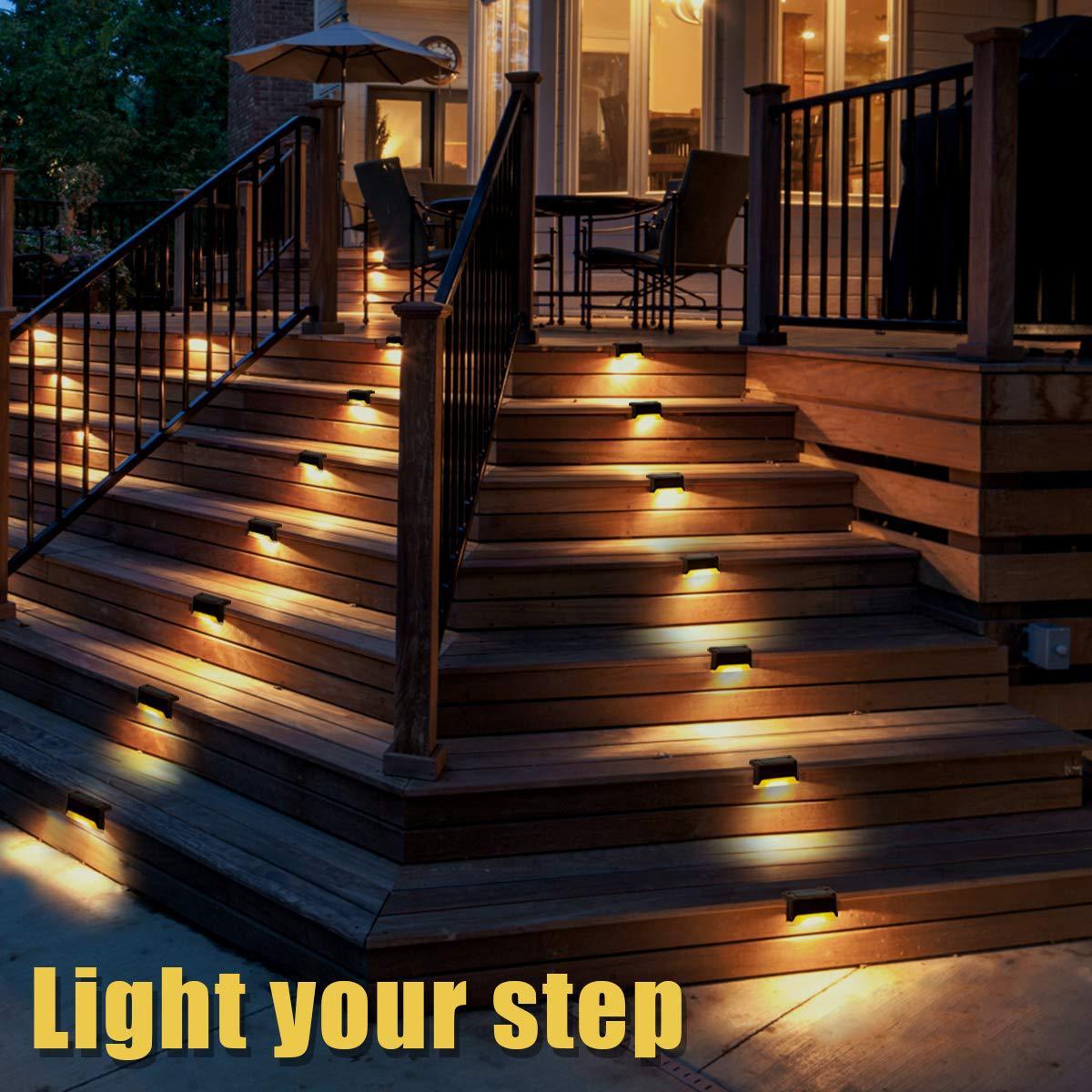 Four solar deck lights installed on a wooden patio, illuminating the pathway with a warm glow, showcasing their waterproof design.