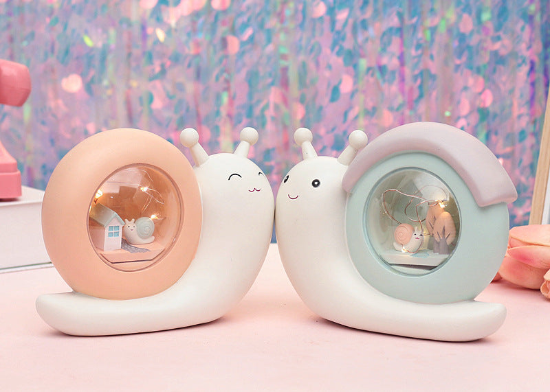 A cute cartoon snail-shaped night lamp and piggy bank in medium blue and yellow colors, perfect for children's rooms.