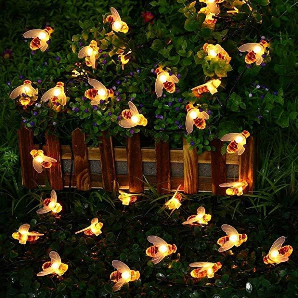 A string of solar-powered LED fairy lights shaped like cute honey bees, illuminating a garden at night.