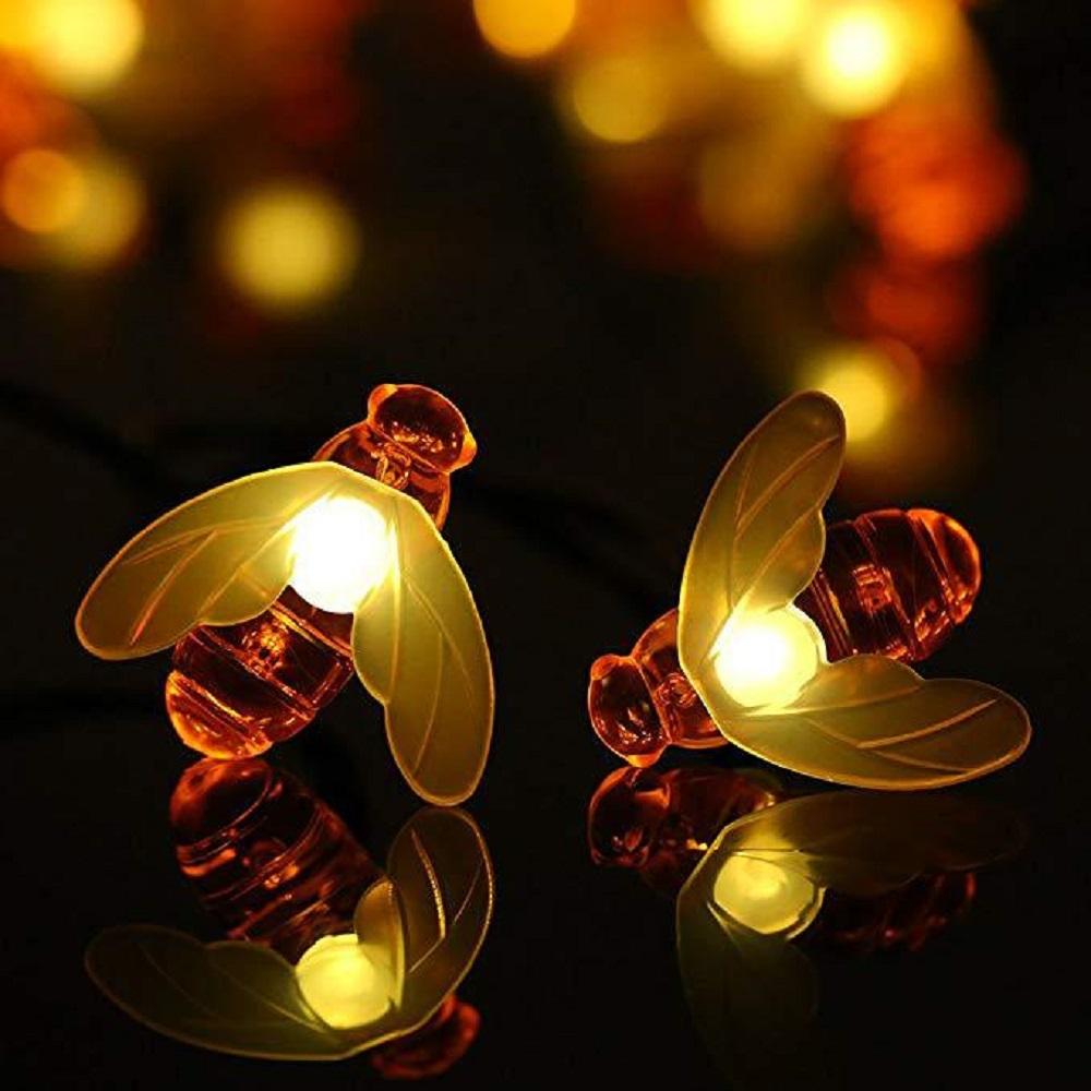 A string of solar-powered LED fairy lights shaped like cute honey bees, illuminating a garden at night.