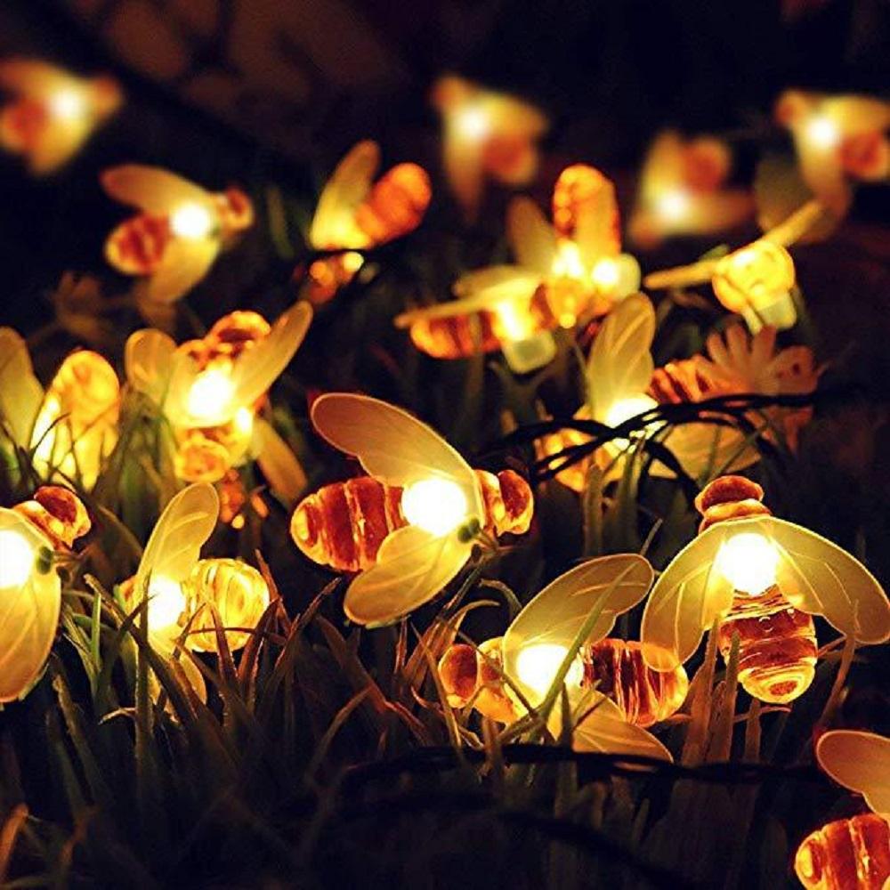A string of solar-powered LED fairy lights shaped like cute honey bees, illuminating a garden at night.