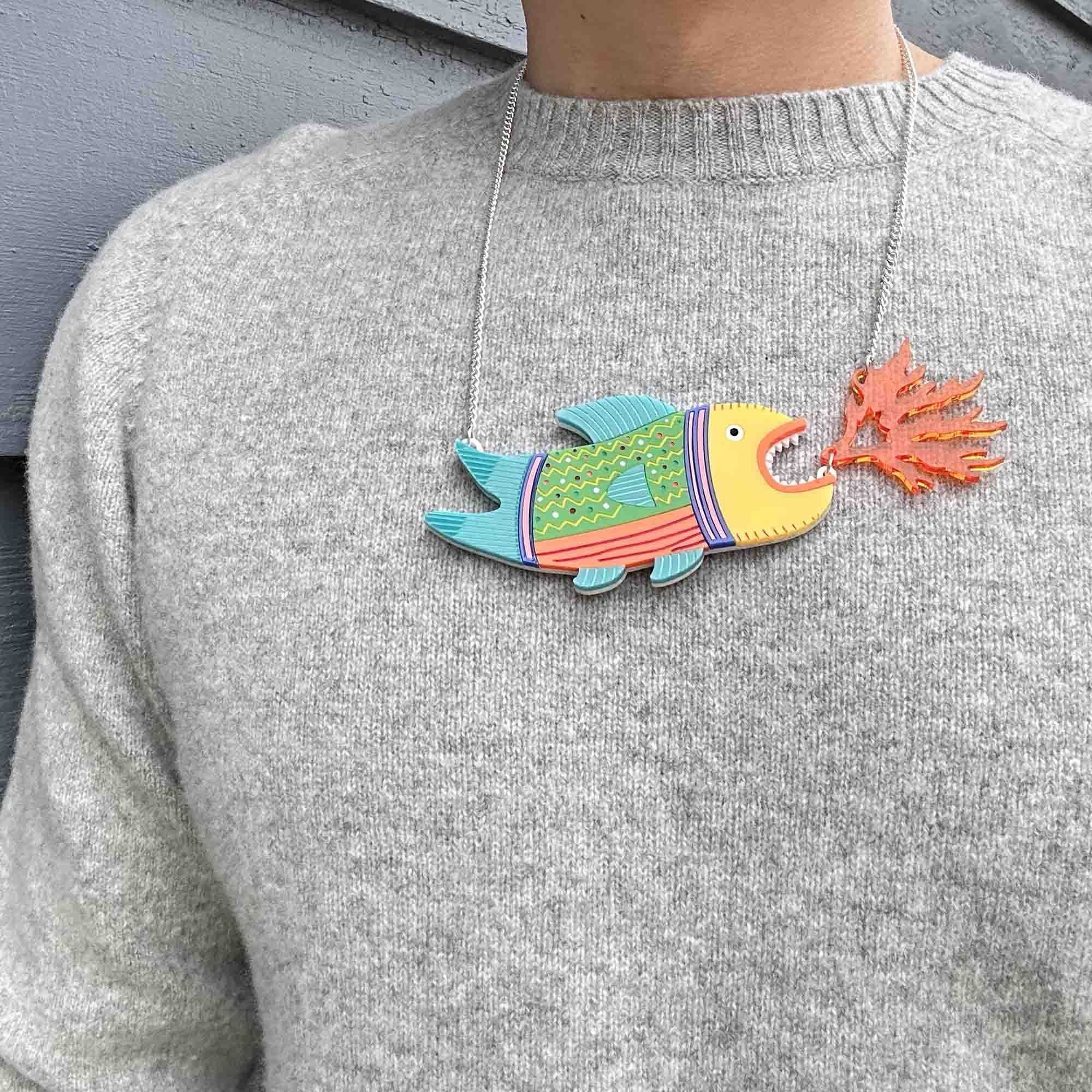 A vibrant Fish and Alligator Necklace featuring laser cut acrylic designs, hand-painted scales, and an articulated flame, hung from a silver plated chain.