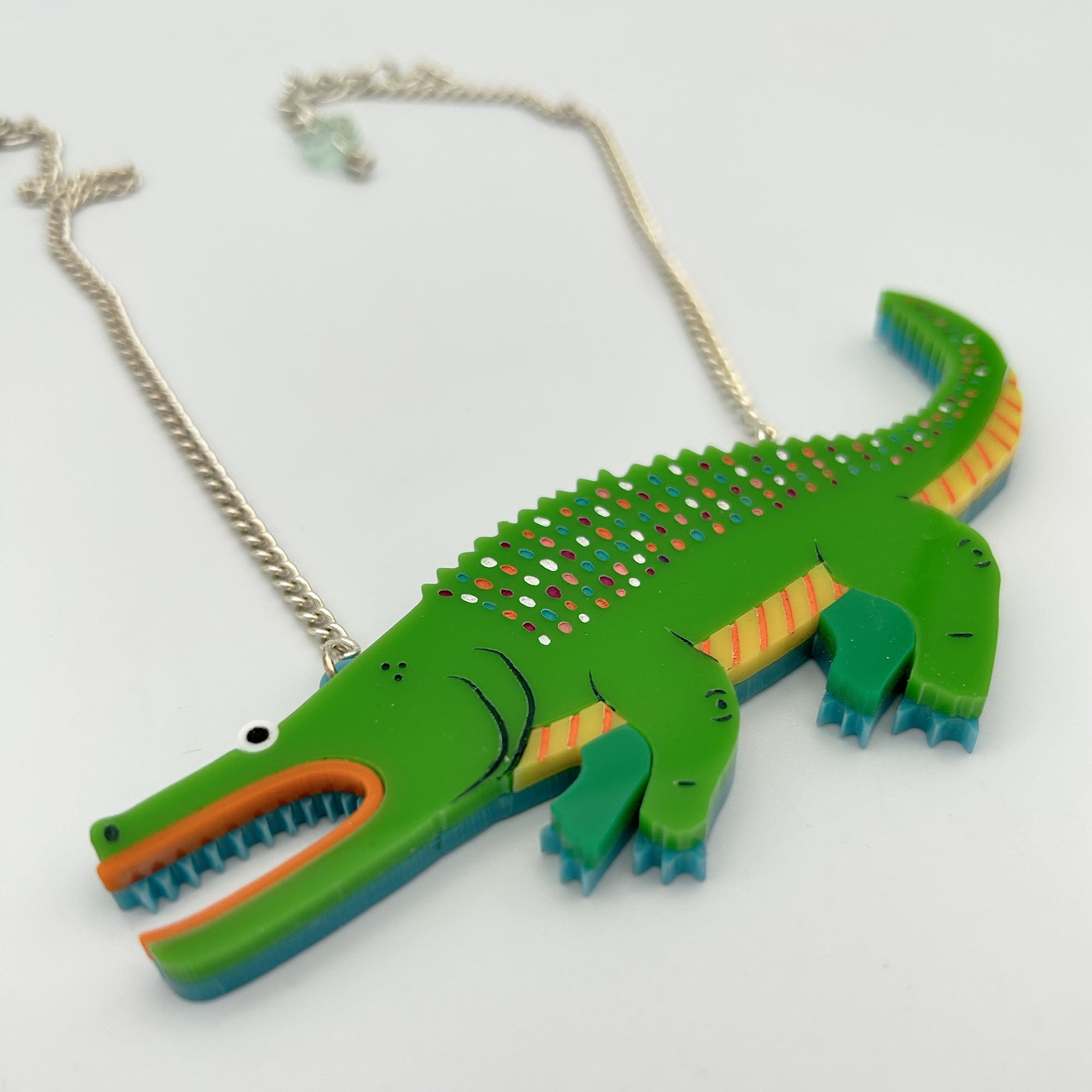 A vibrant Fish and Alligator Necklace featuring laser cut acrylic designs, hand-painted scales, and an articulated flame, hung from a silver plated chain.