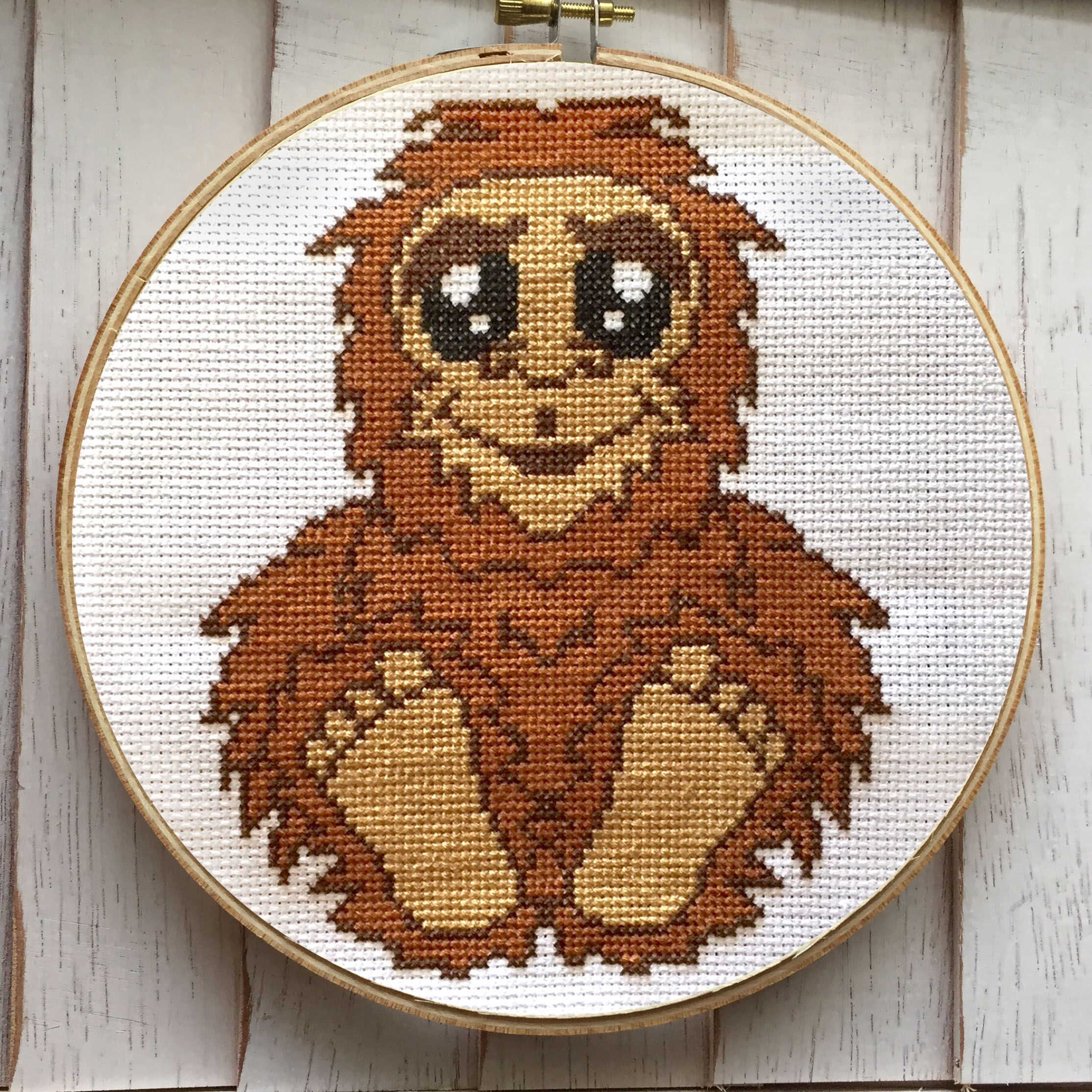 A DIY counted cross stitch kit featuring a Bigfoot Sasquatch design, including supplies like fabric, threads, and a wooden hoop.