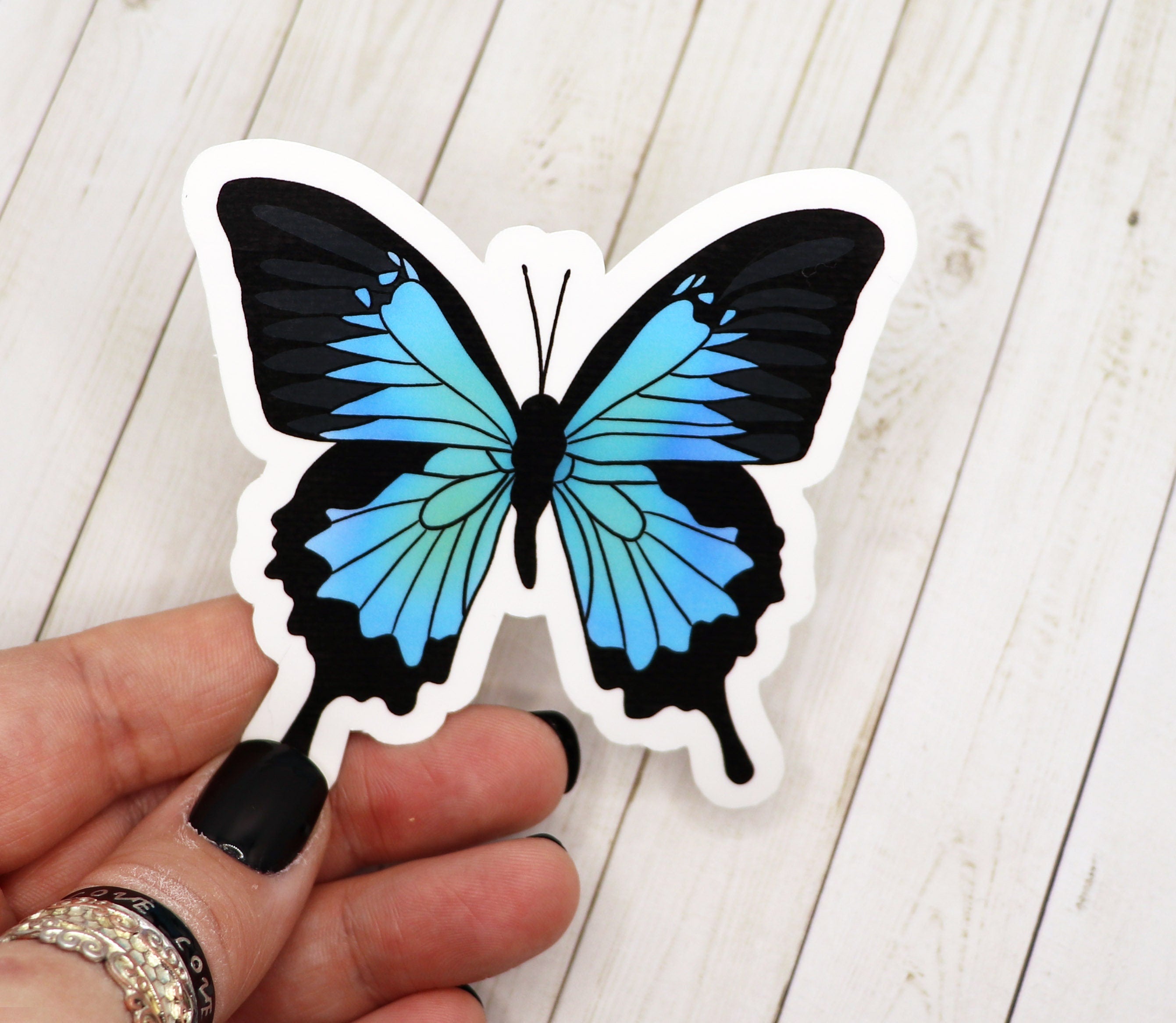A vibrant blue butterfly sticker on a white background, showcasing its intricate design and matte finish.