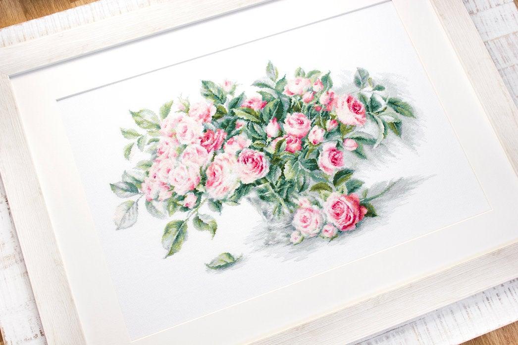 A counted cross-stitch kit featuring a bouquet of pink roses, including canvas, threads, needle, and instructions.