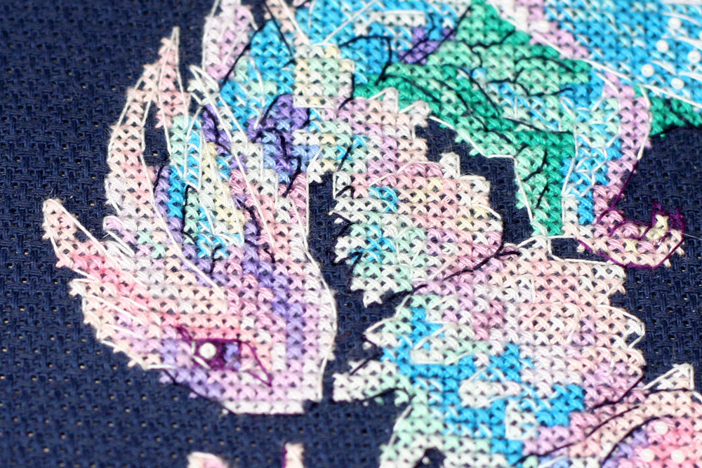 Cross-stitch kit featuring a Baby Dragon design with dark blue canvas, colorful floss, and beads.