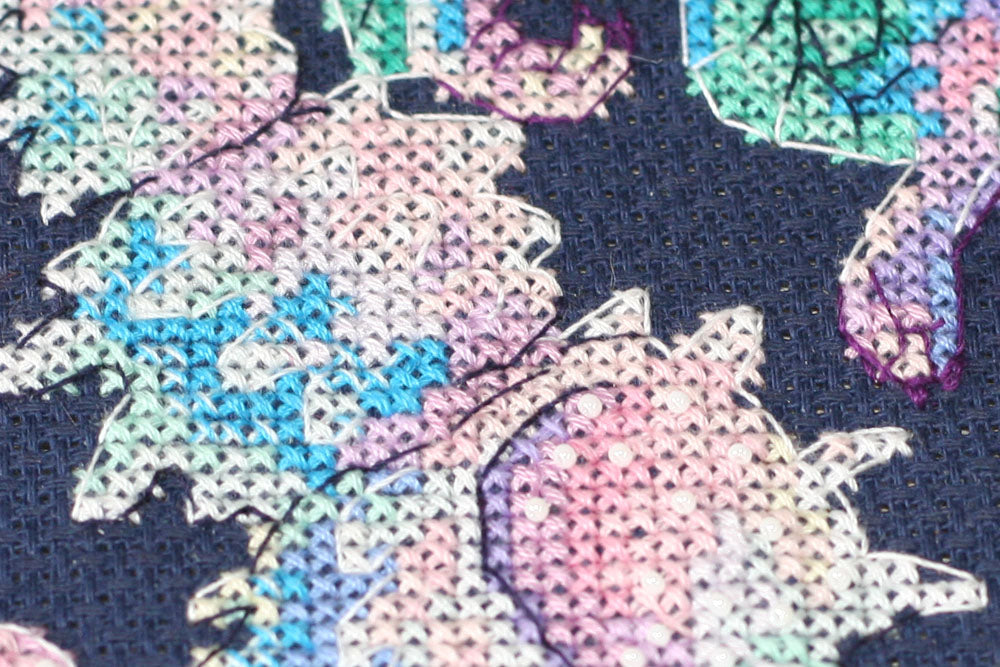 Cross-stitch kit featuring a Baby Dragon design with dark blue canvas, colorful floss, and beads.