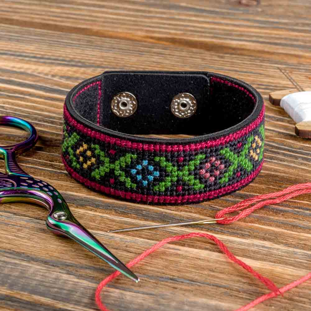 Cross-stitch kit on artificial leather FLHL-028 with materials for creating a bracelet, including cotton floss and needle.