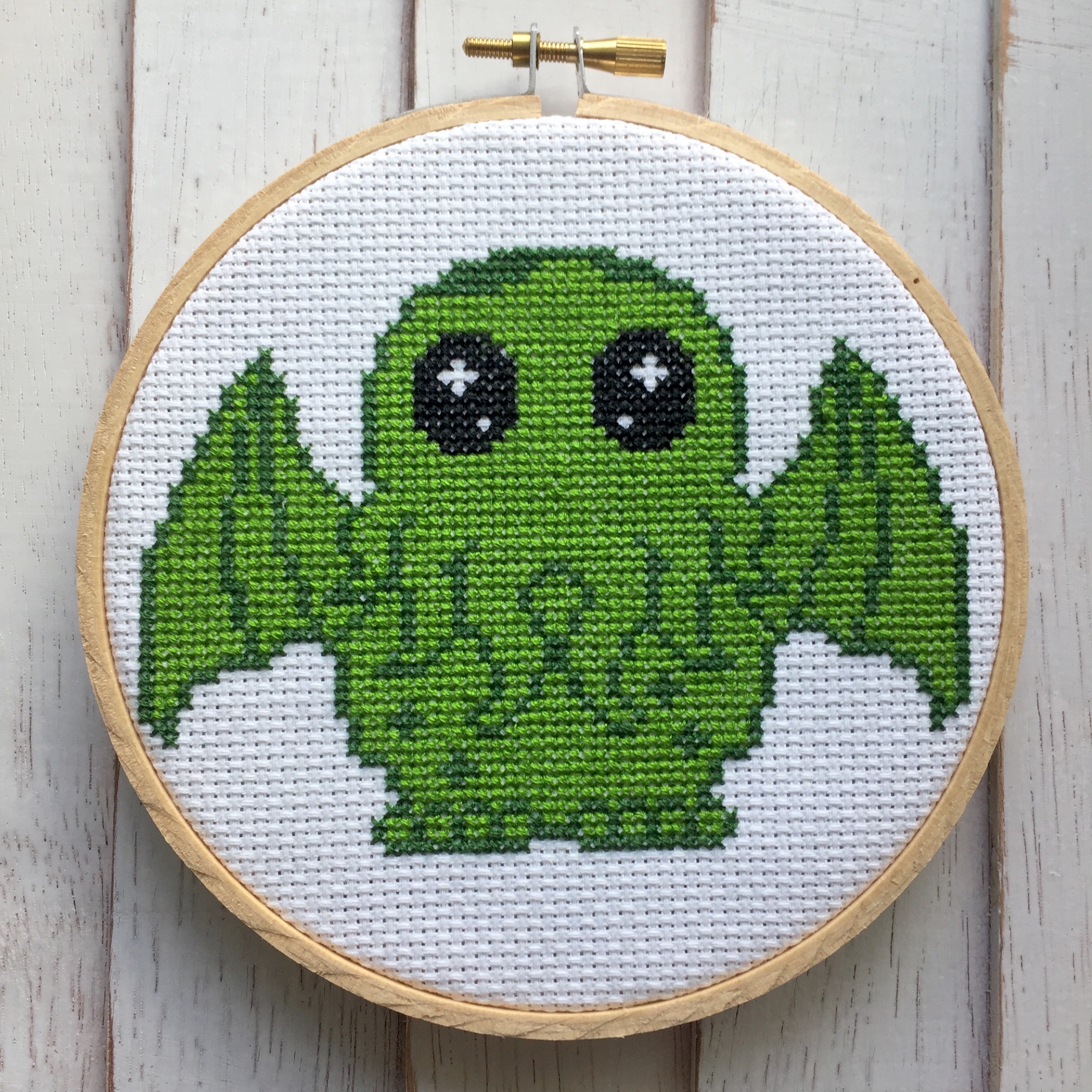 A colorful Cute Cthulhu counted cross stitch kit featuring a 5-inch design, complete with threads, fabric, needle, and wood hoop.