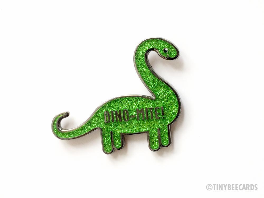 A glittery green brontosaurus enamel pin with the text 'Dino-mite!' designed for accessories and gifts.