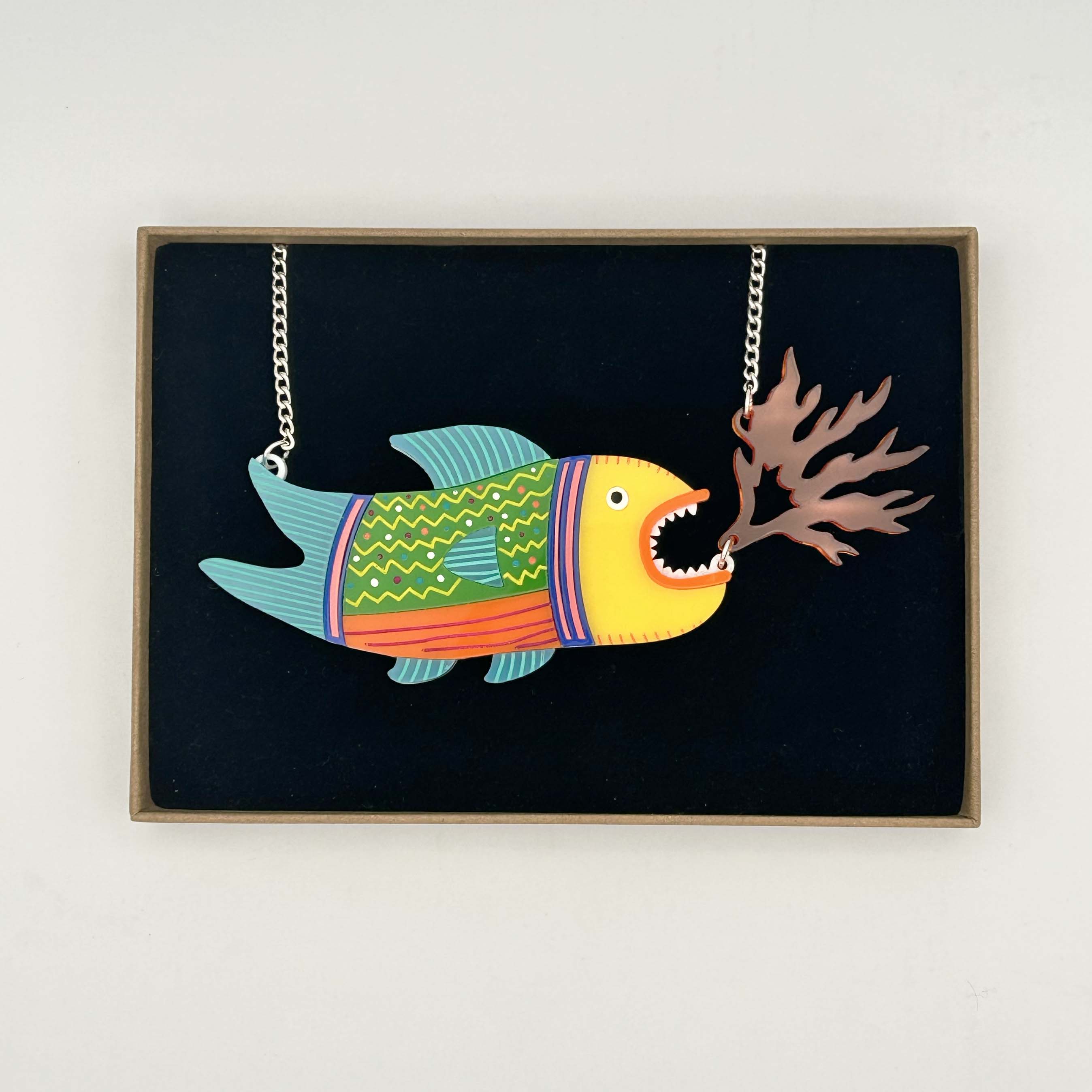 A vibrant Fire-Breathing Fish Necklace featuring laser-cut acrylic with hand-painted details and a transparent orange flame, displayed elegantly.