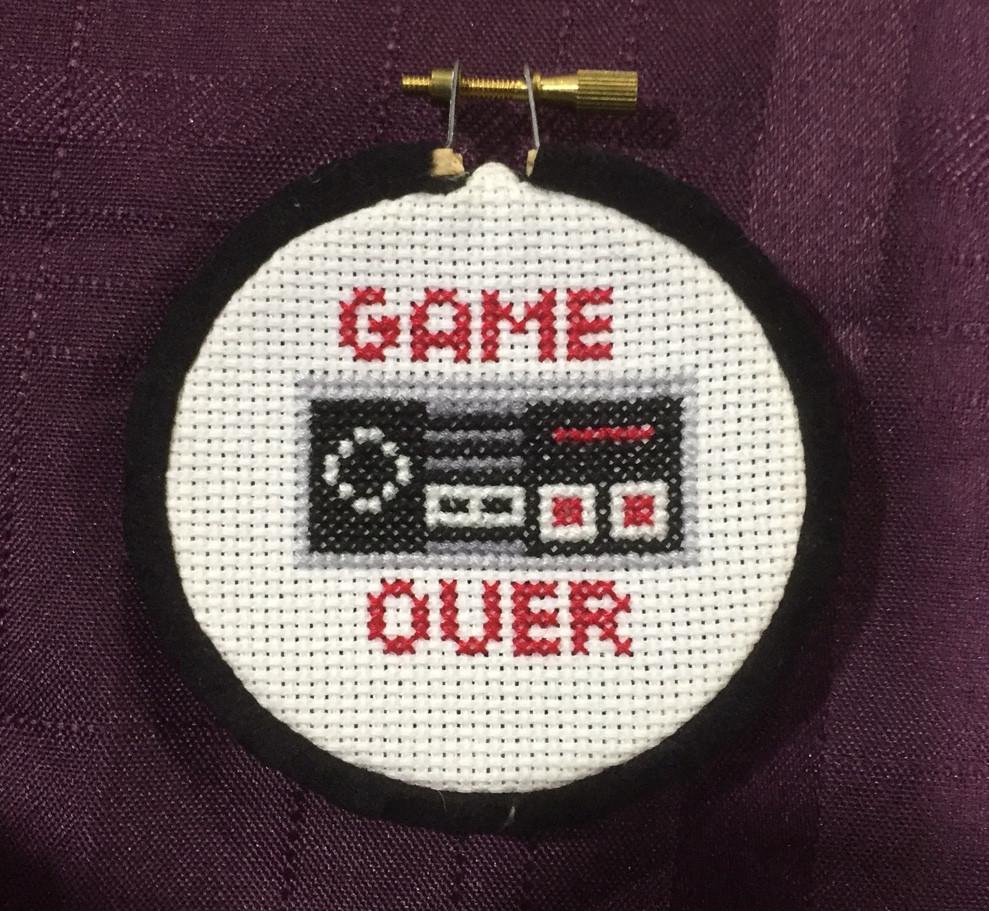 Game Over Controller Counted Cross Stitch DIY Kit featuring a vintage Nintendo controller design with black Aida fabric and colorful DMC threads.