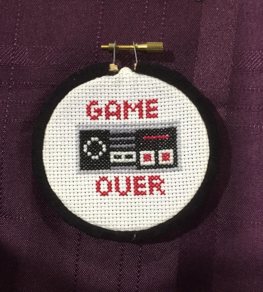 Game Over Controller Counted Cross Stitch DIY Kit featuring a vintage Nintendo controller design with black Aida fabric and colorful DMC threads.