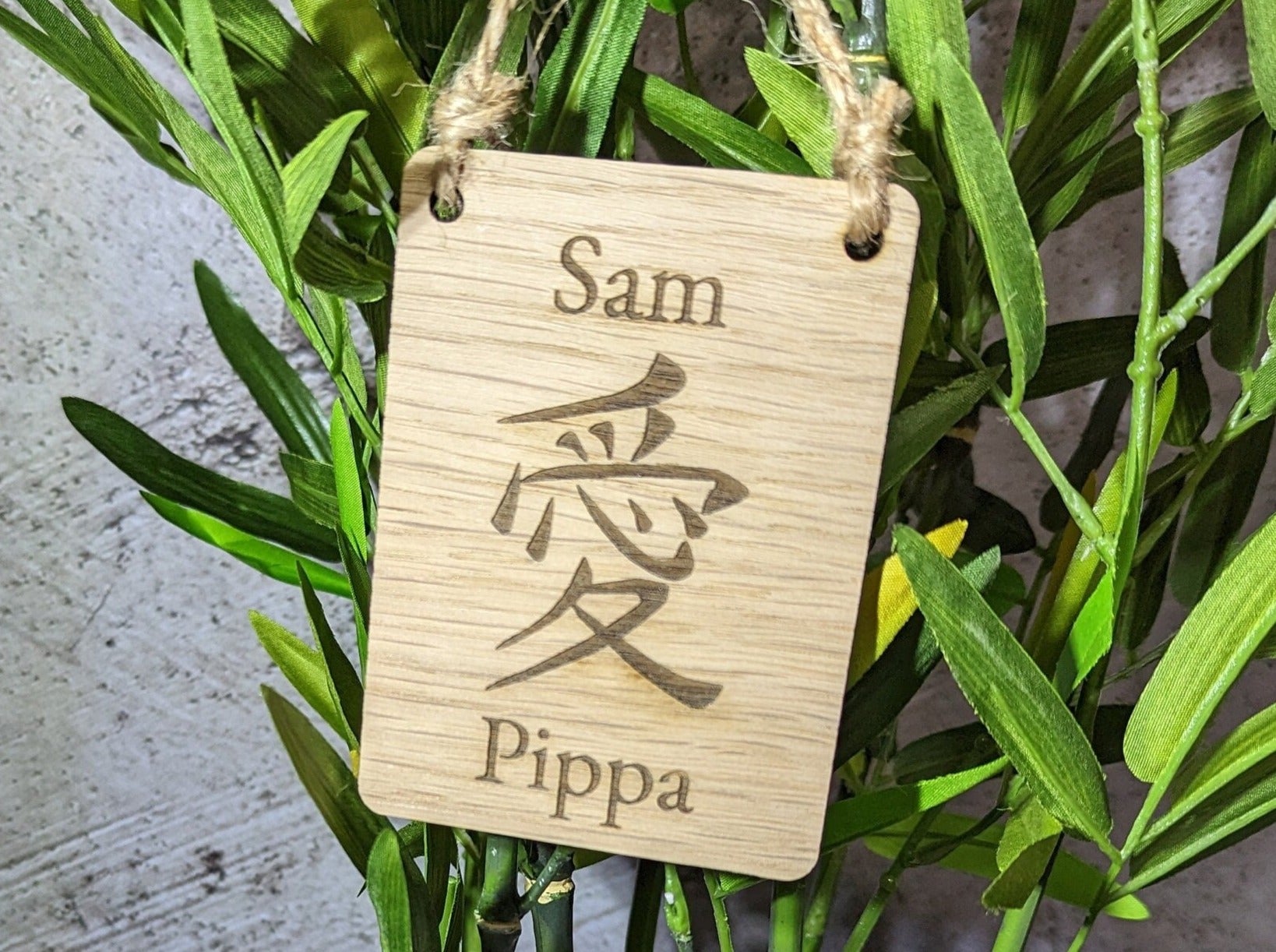 Personalised wooden Japanese sign with engraved names and characters, hanging with rustic jute string.