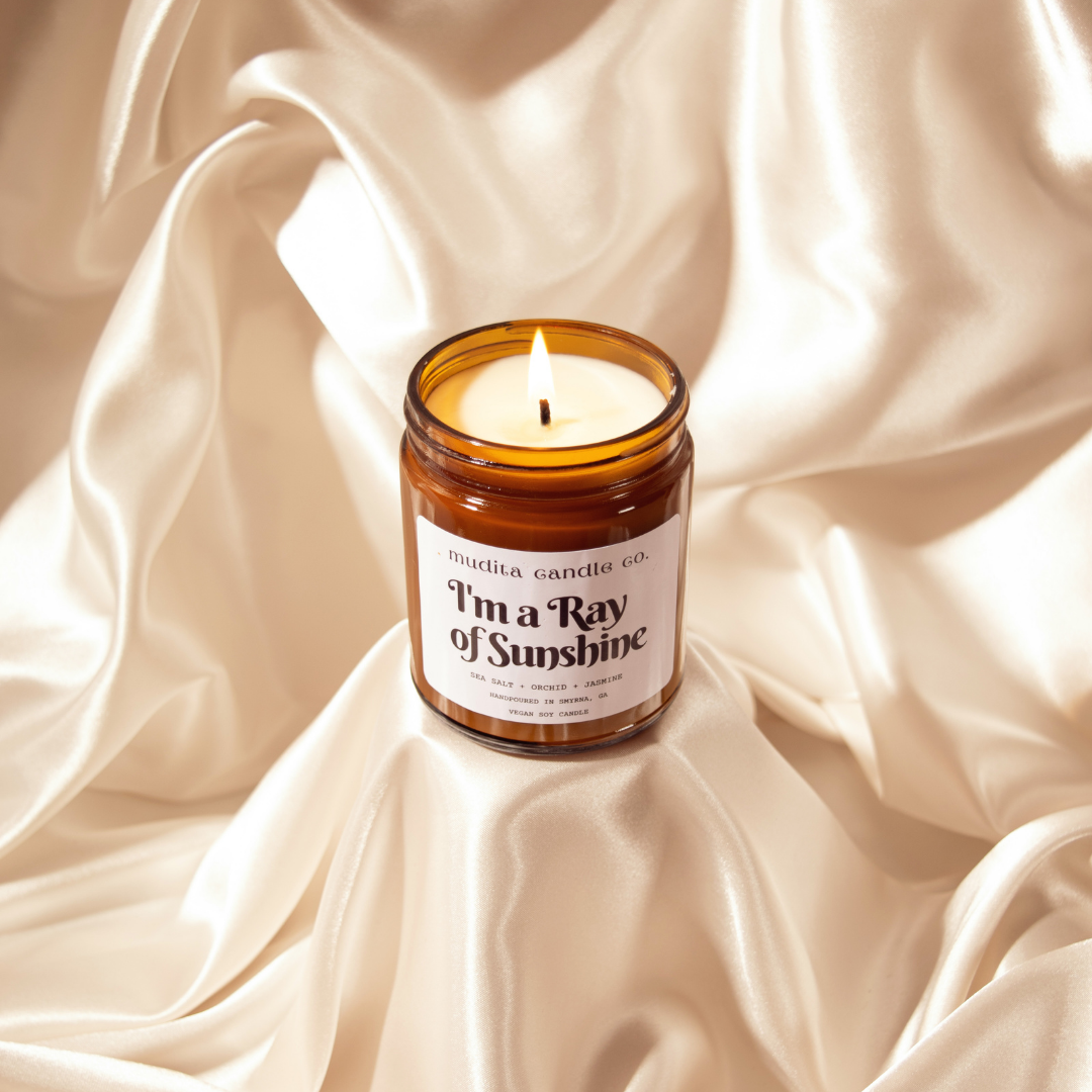 I'm A Ray of Sunshine soy candle in amber glass jar with gold lid, featuring sea salt, orchid, and jasmine scents.
