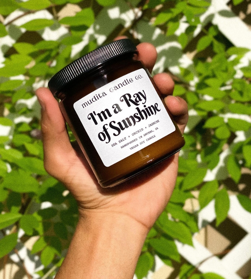 I'm A Ray of Sunshine soy candle in amber glass jar with gold lid, featuring sea salt, orchid, and jasmine scents.