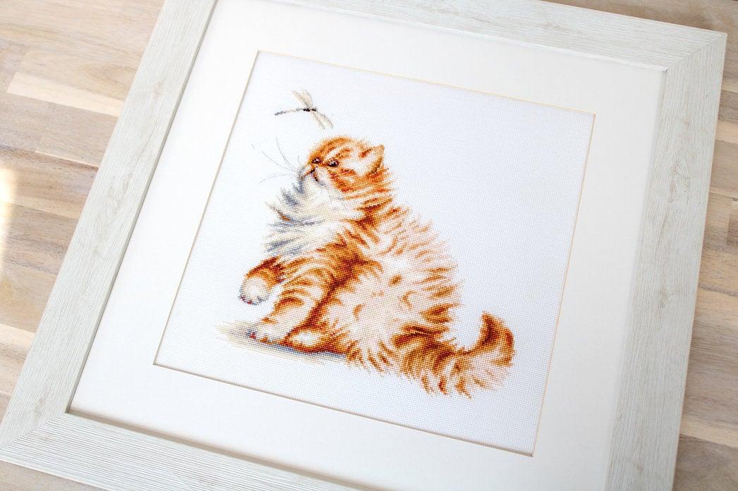 Counted cross-stitch kit featuring a ginger Persian kitten playing with a dragonfly, includes canvas, threads, and needle.