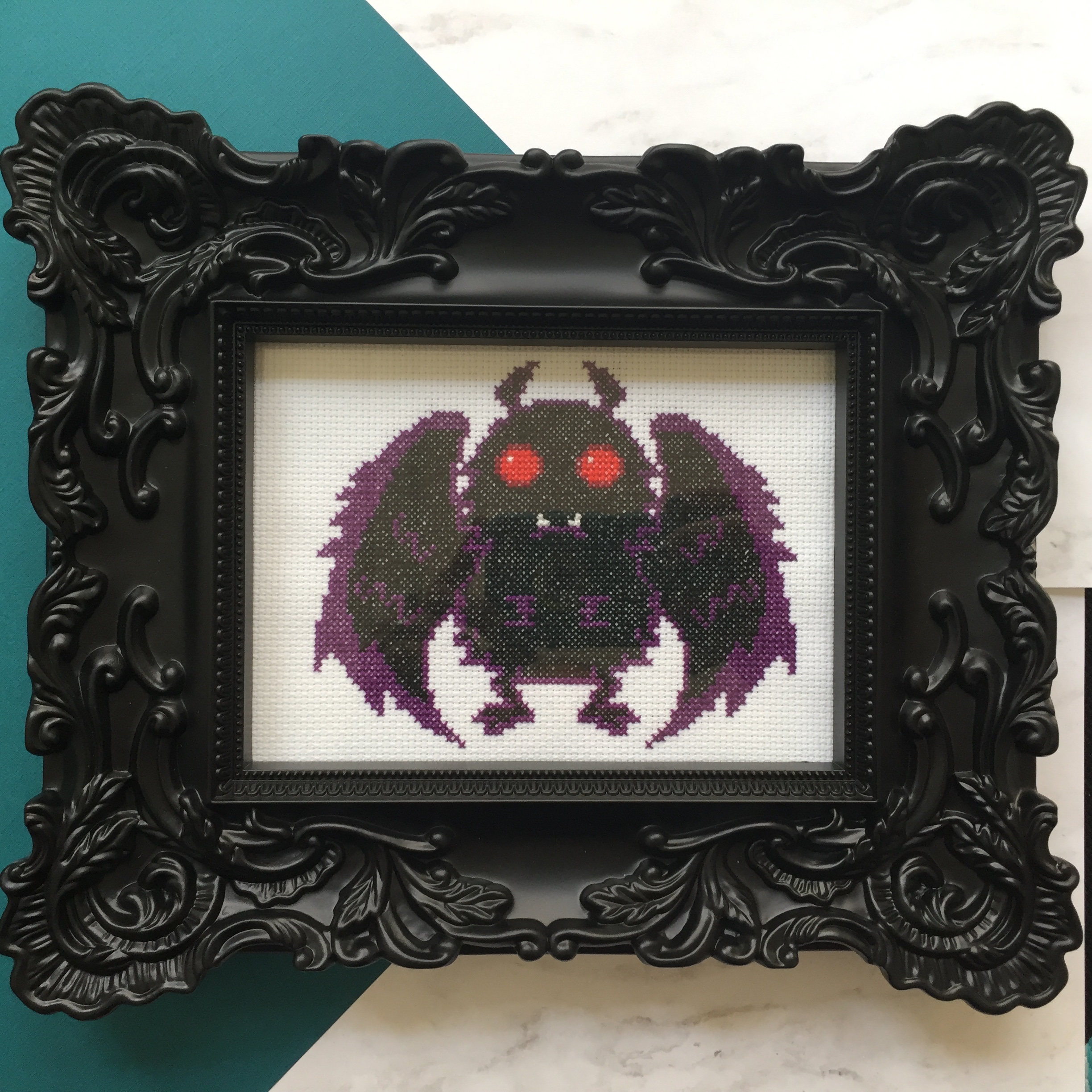 Mothman Counted Cross Stitch DIY Kit featuring supplies like fabric, threads, and a wood hoop.