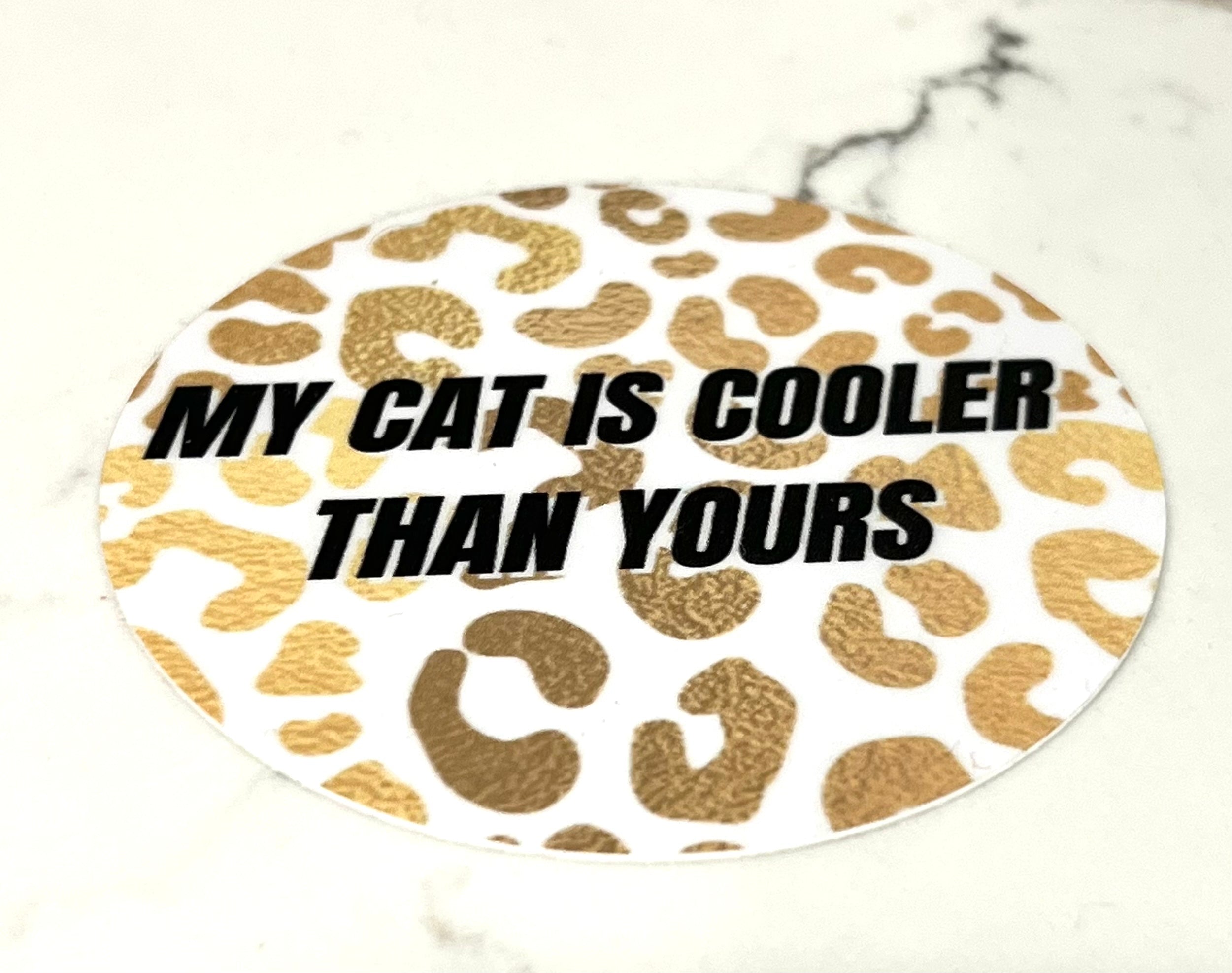 A 3-inch vinyl circle sticker featuring the phrase 'MY CAT IS COOLER THAN YOURS' with a playful design, perfect for cat lovers.