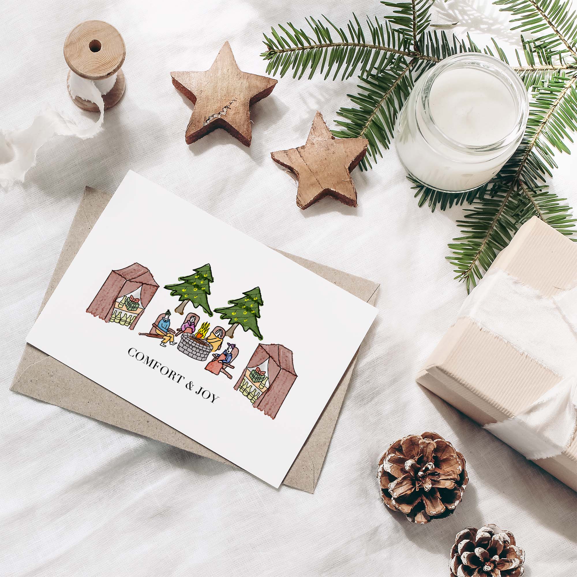 Outdoor Christmas greeting card set featuring a hand-drawn campfire scene with four people, packaged in a clear plastic box.