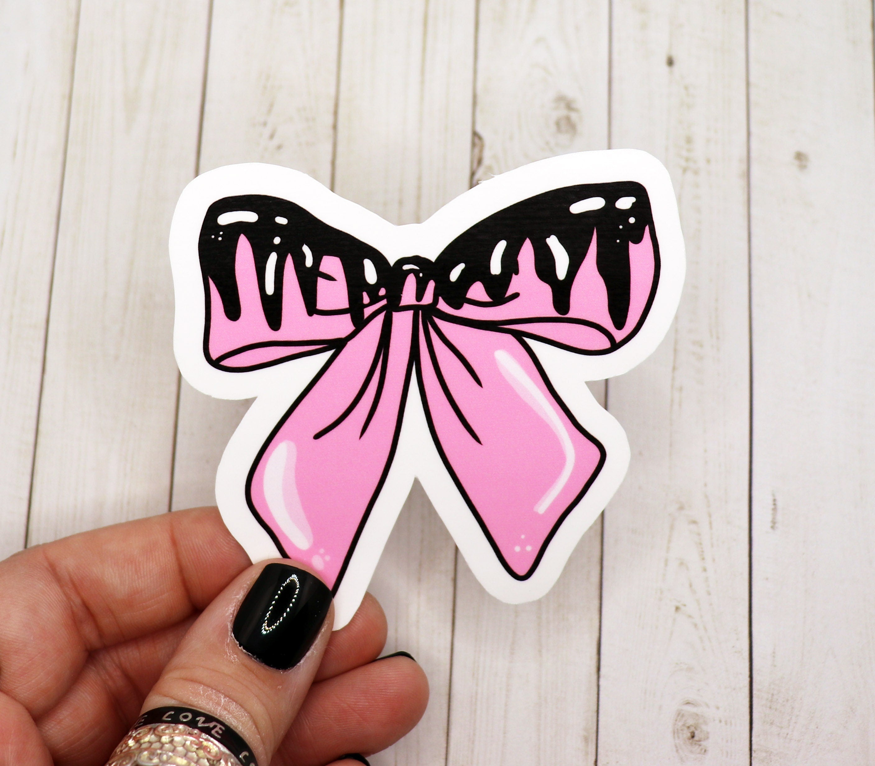 A pastel goth pink bow sticker on a white background, showcasing its vibrant color and matte finish.