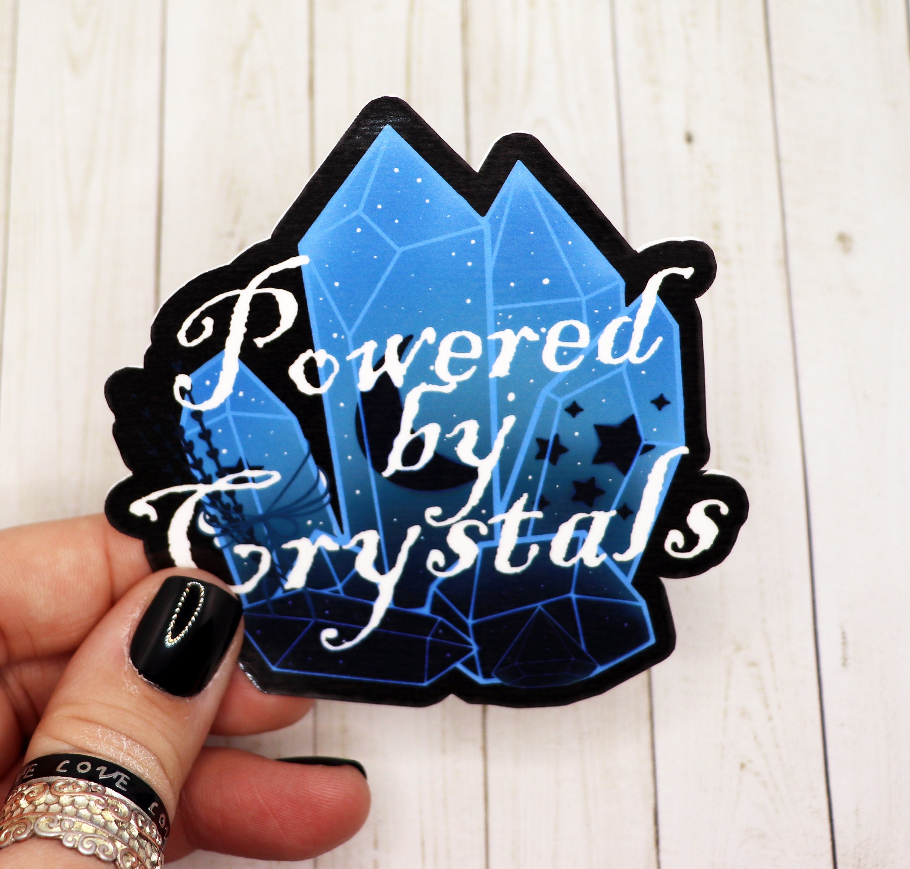 A vibrant 'Powered by Crystals' sticker on a matte vinyl surface, showcasing its colorful design and 2.5-inch size.