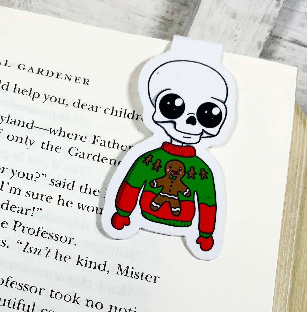 A colorful bookmark featuring a skeleton in an ugly Christmas sweater, showcasing a festive design perfect for holiday reading.