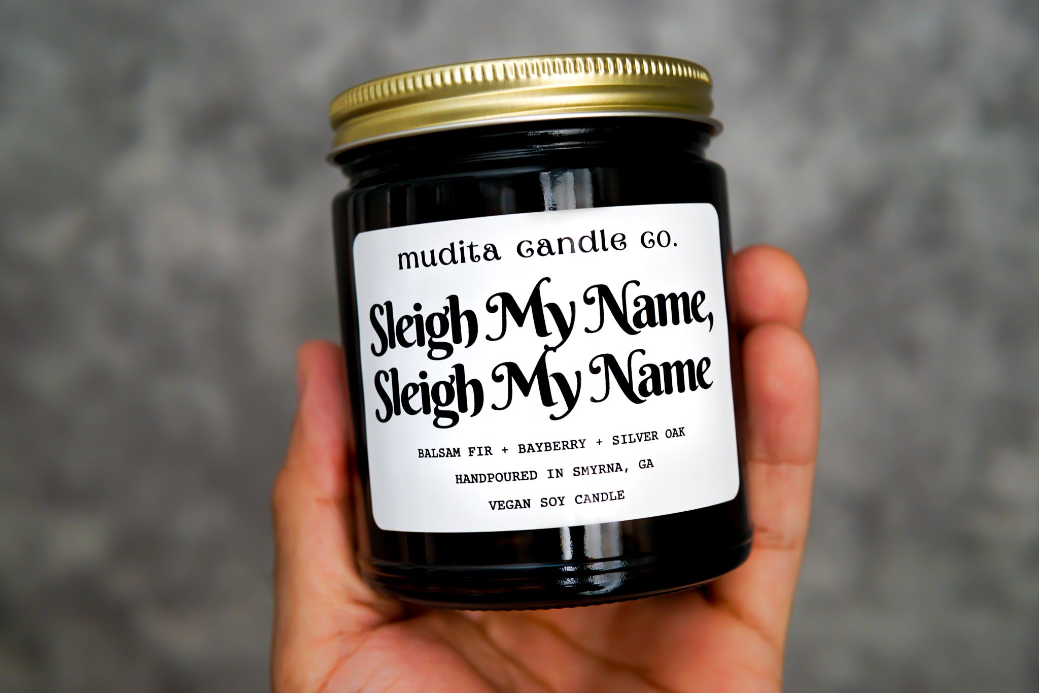 Sleight My Name, Sleigh My Name candle in amber glass jar with gold lid, featuring a festive fragrance blend of Bayberry, Silver Oak, and Balsam Fir.