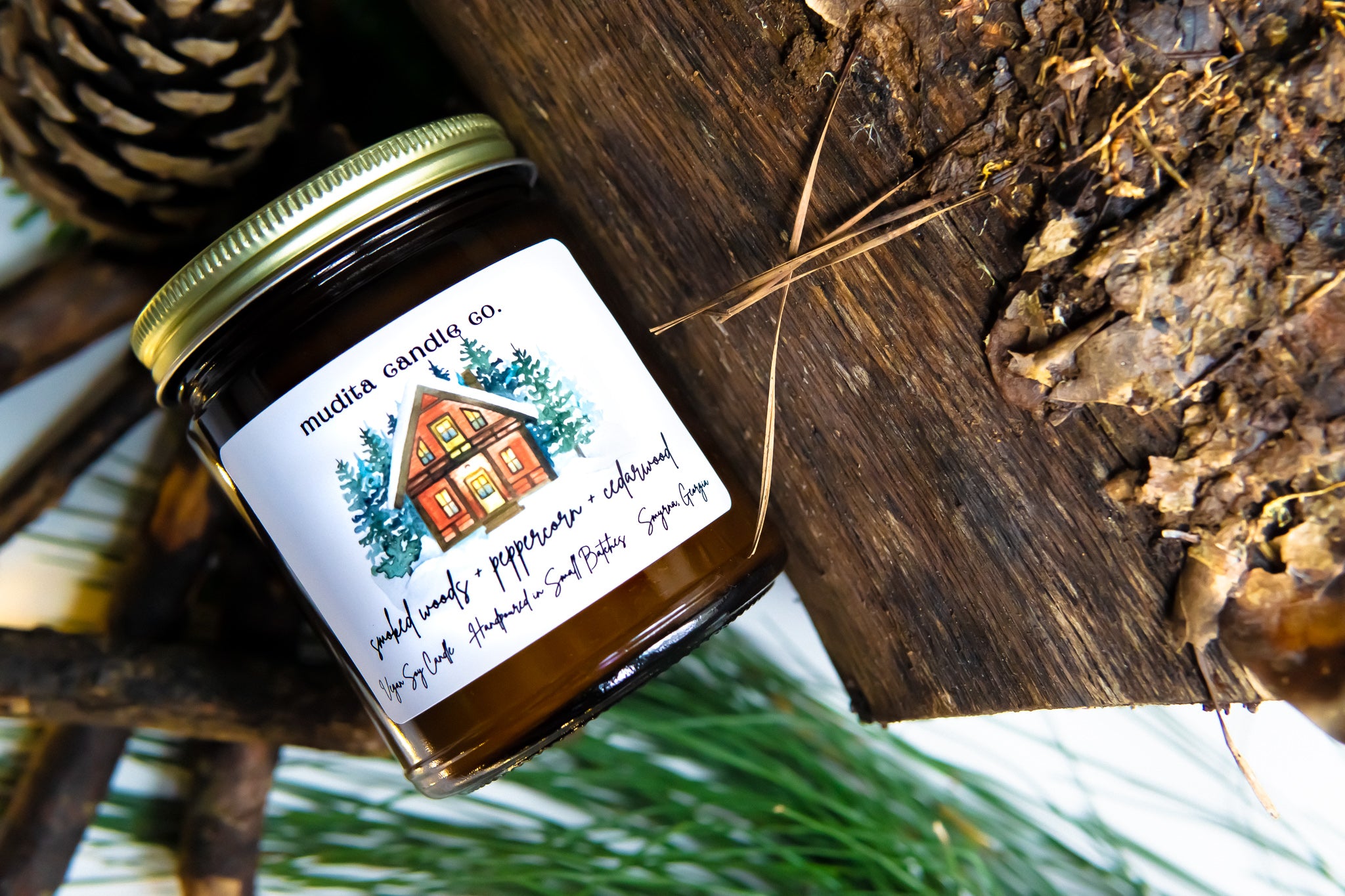 A beautifully crafted 9oz amber glass candle jar with a gold metal lid, featuring the fragrance blend of Smoked Woods, Peppercorn, and Cedarwood.