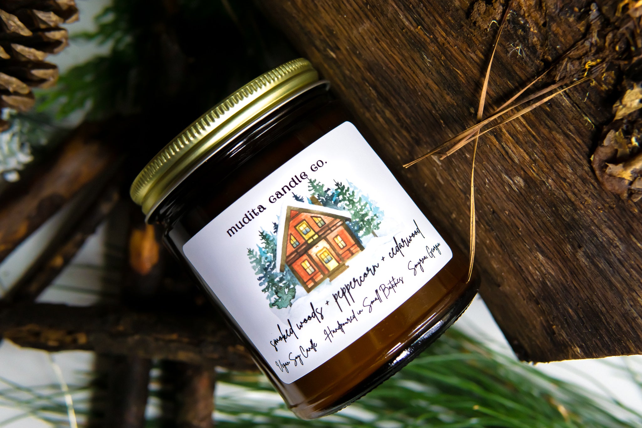 A beautifully crafted 9oz amber glass candle jar with a gold metal lid, featuring the fragrance blend of Smoked Woods, Peppercorn, and Cedarwood.