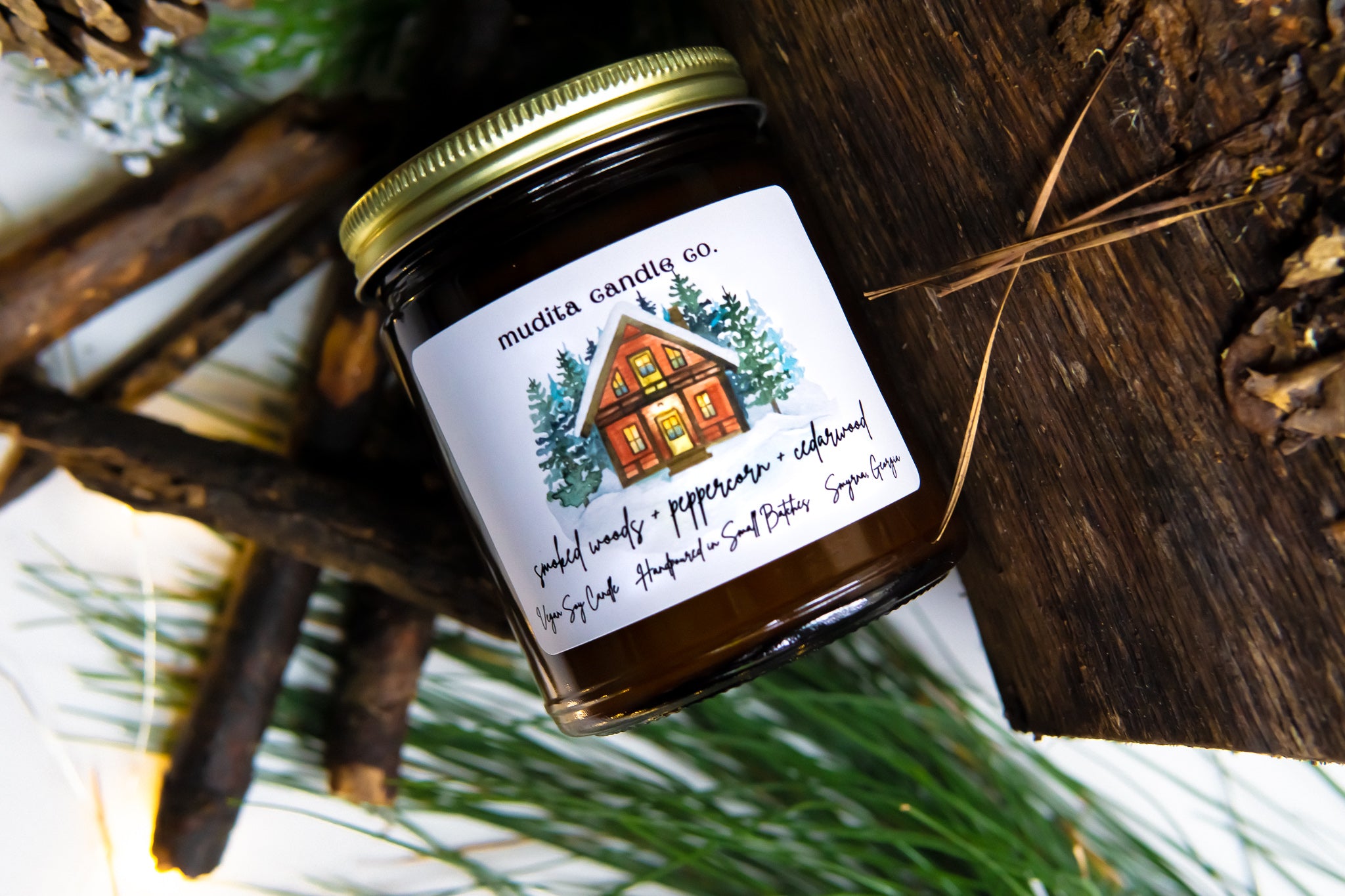 A beautifully crafted 9oz amber glass candle jar with a gold metal lid, featuring the fragrance blend of Smoked Woods, Peppercorn, and Cedarwood.